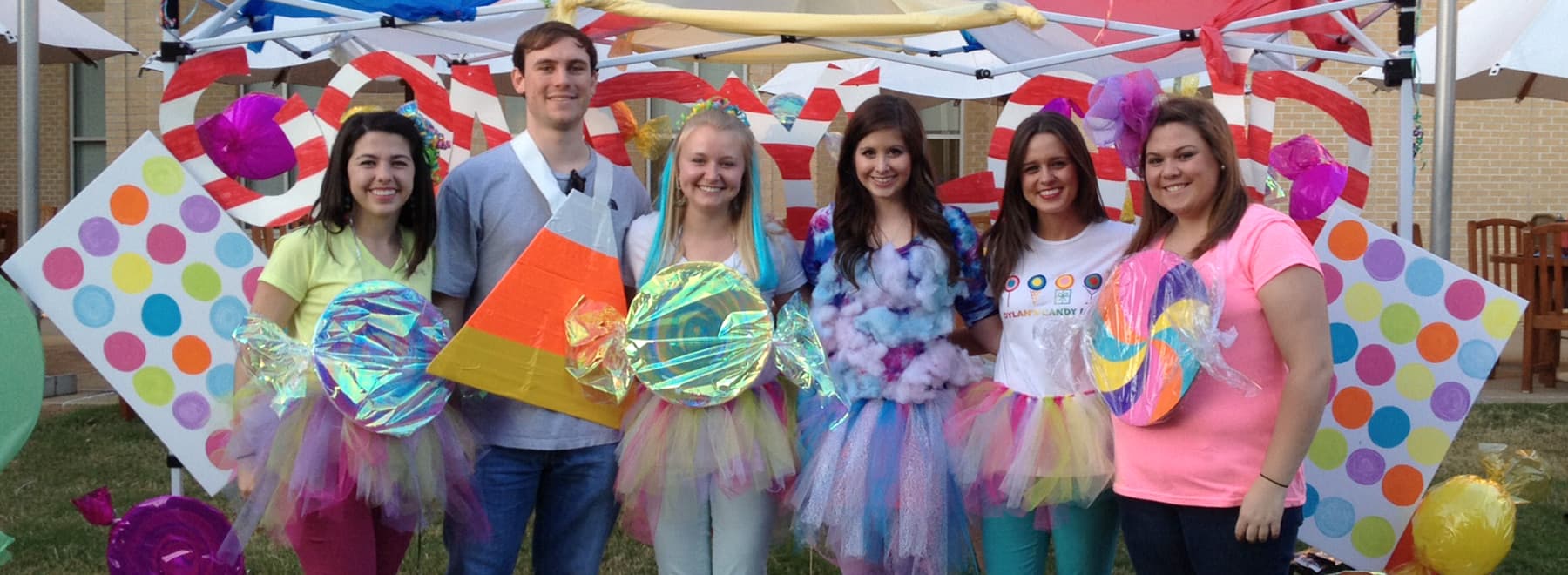Group of male and female students pose for candy land event in colorful costumes.